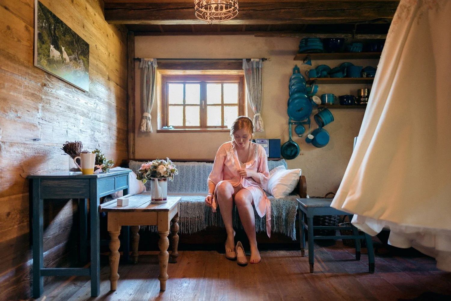 Nevěsta v růžovém županu si obouvá střevíc v rustikální místnosti s modrým nádobím.