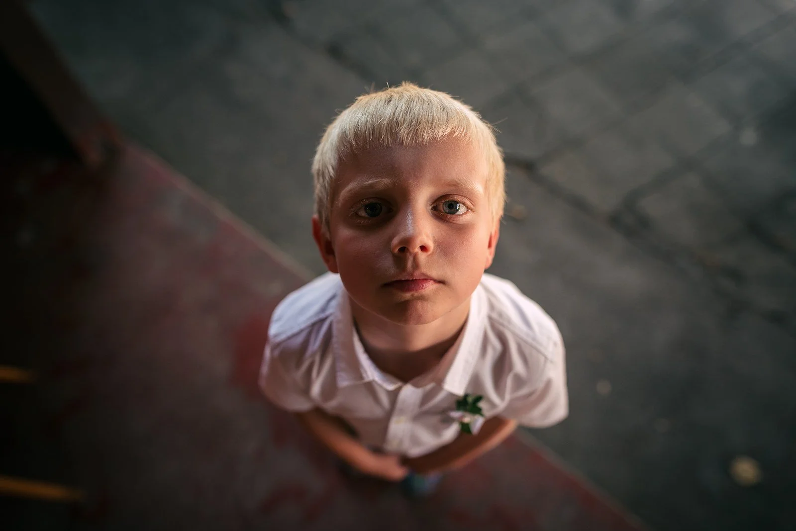 Dítě hledí vzhůru do fotoaparátu z kamenné dlažby.