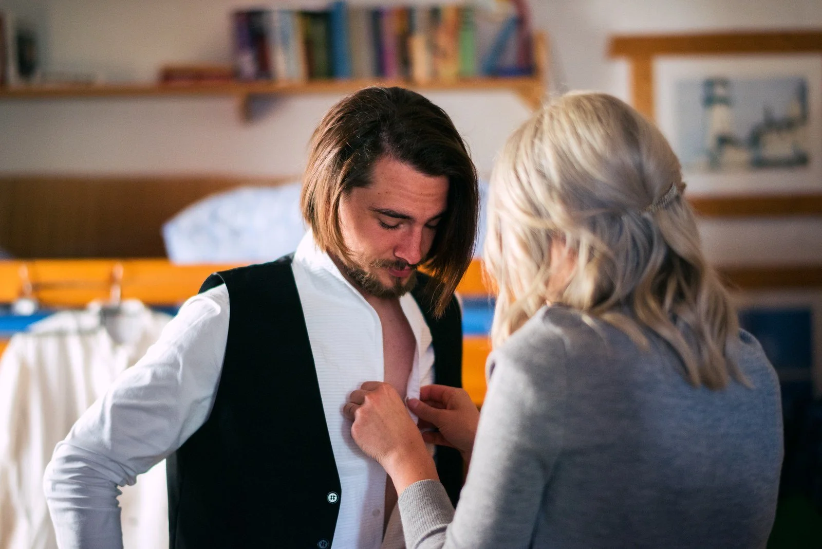 Žena upravuje muži v bílé košili a černé vestě přední část oděvu.