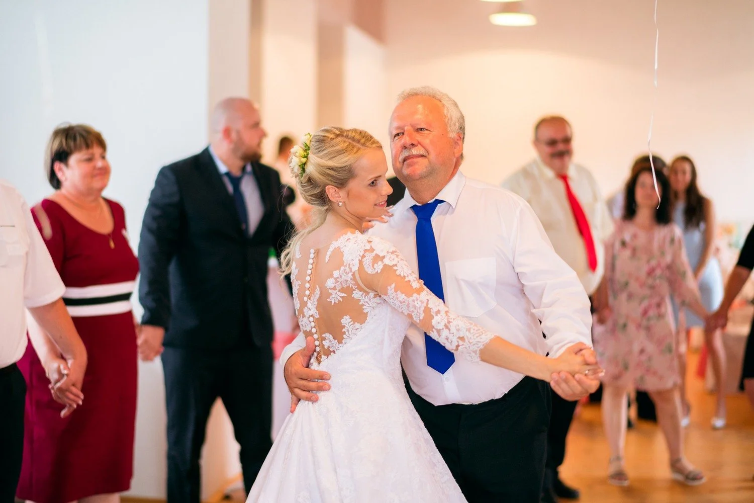Jitka tančí s mužem v bílé košili a modré kravatě, kolem nich se drží hosté za ruce.