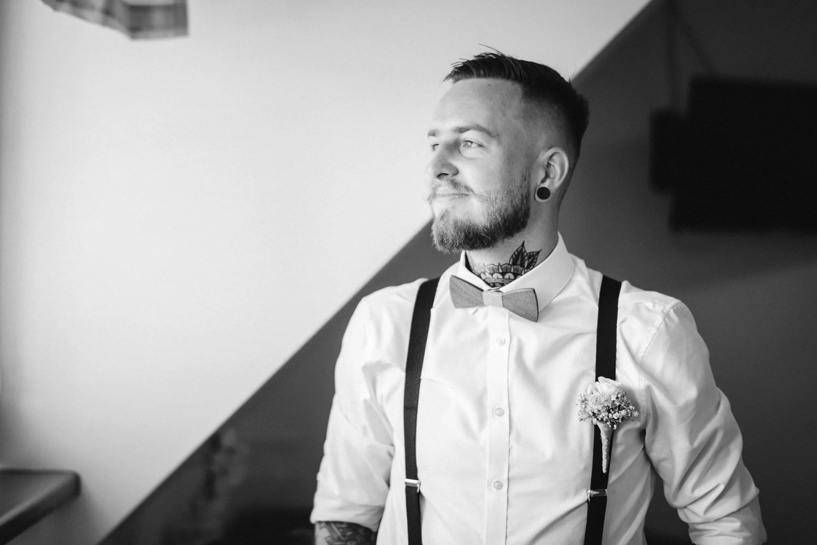 Lukáš stojí v bílé košili u okna a zapíná si manžetový knoflíček.