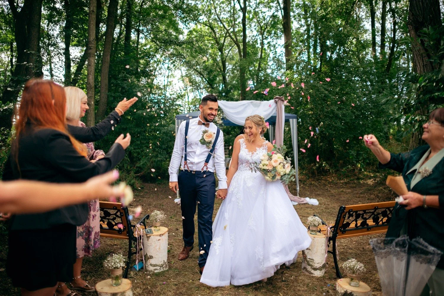Nevěsta a ženich odcházejí uličkou mezi tleskajícími hosty.