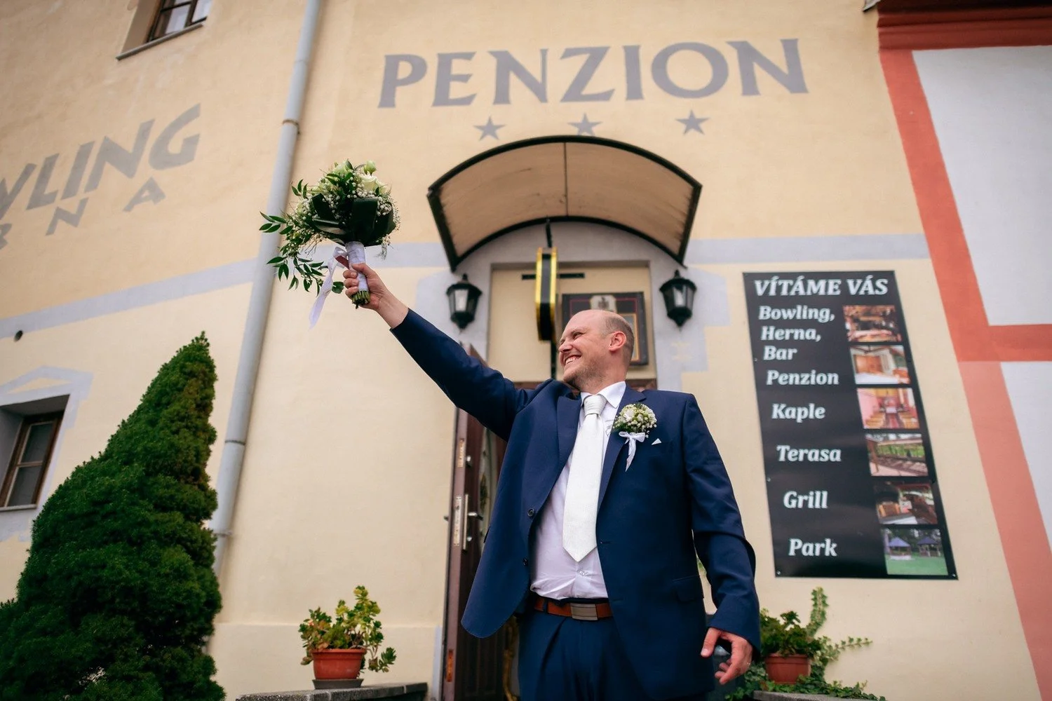 Ženich zvedá kytici před vstupem do penzionu.