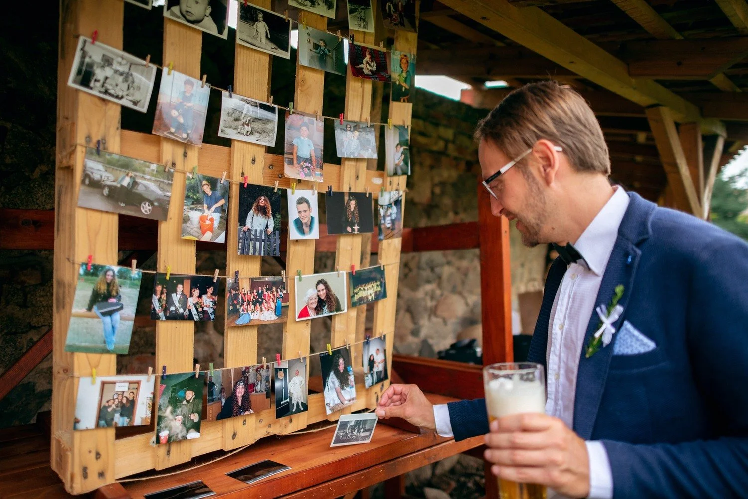 Ženich si prohlíží nástěnku zaplněnou drobnými fotografiemi.