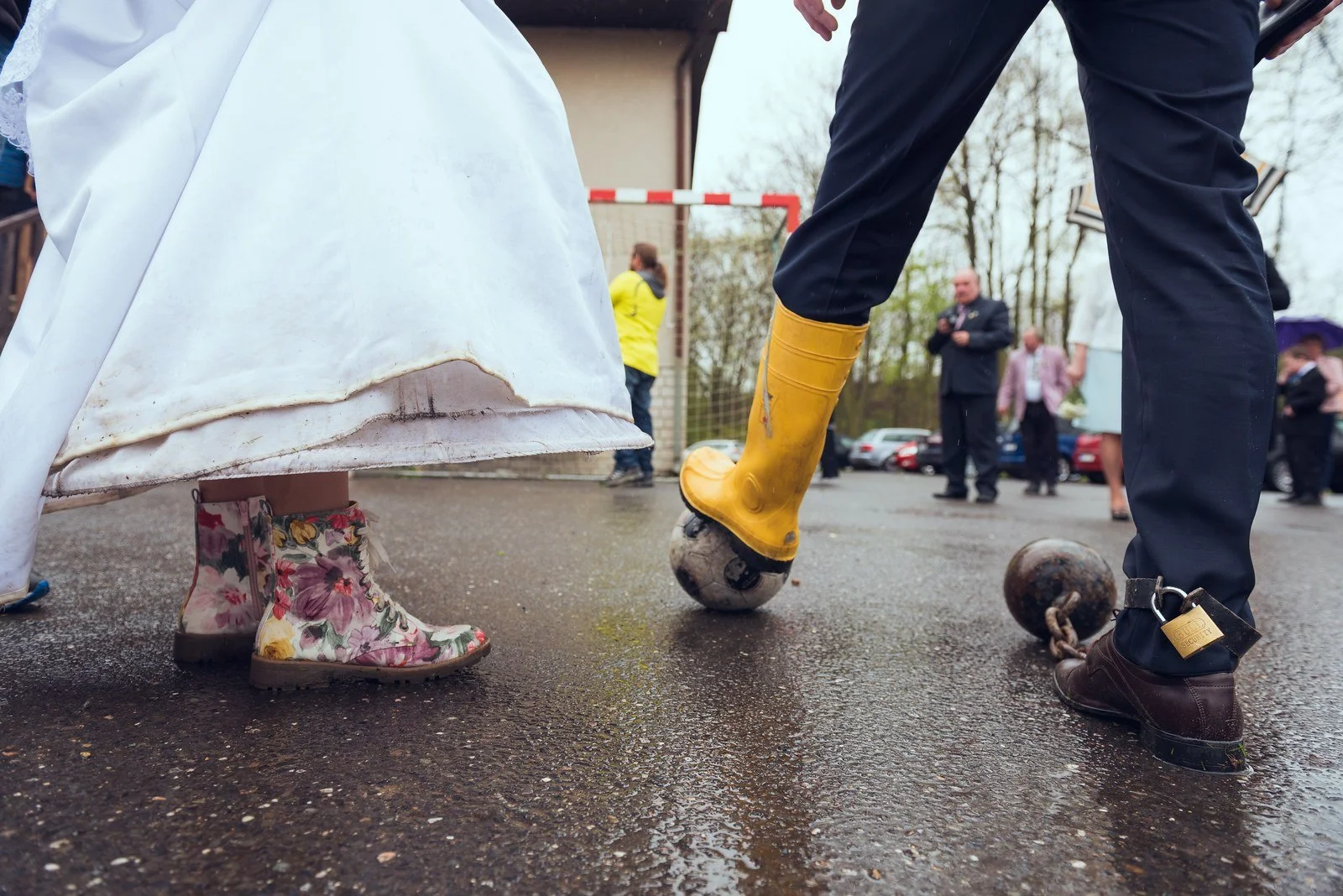 Detail žlutých holínek kráčejících po mokré cestě vedle společenských bot.