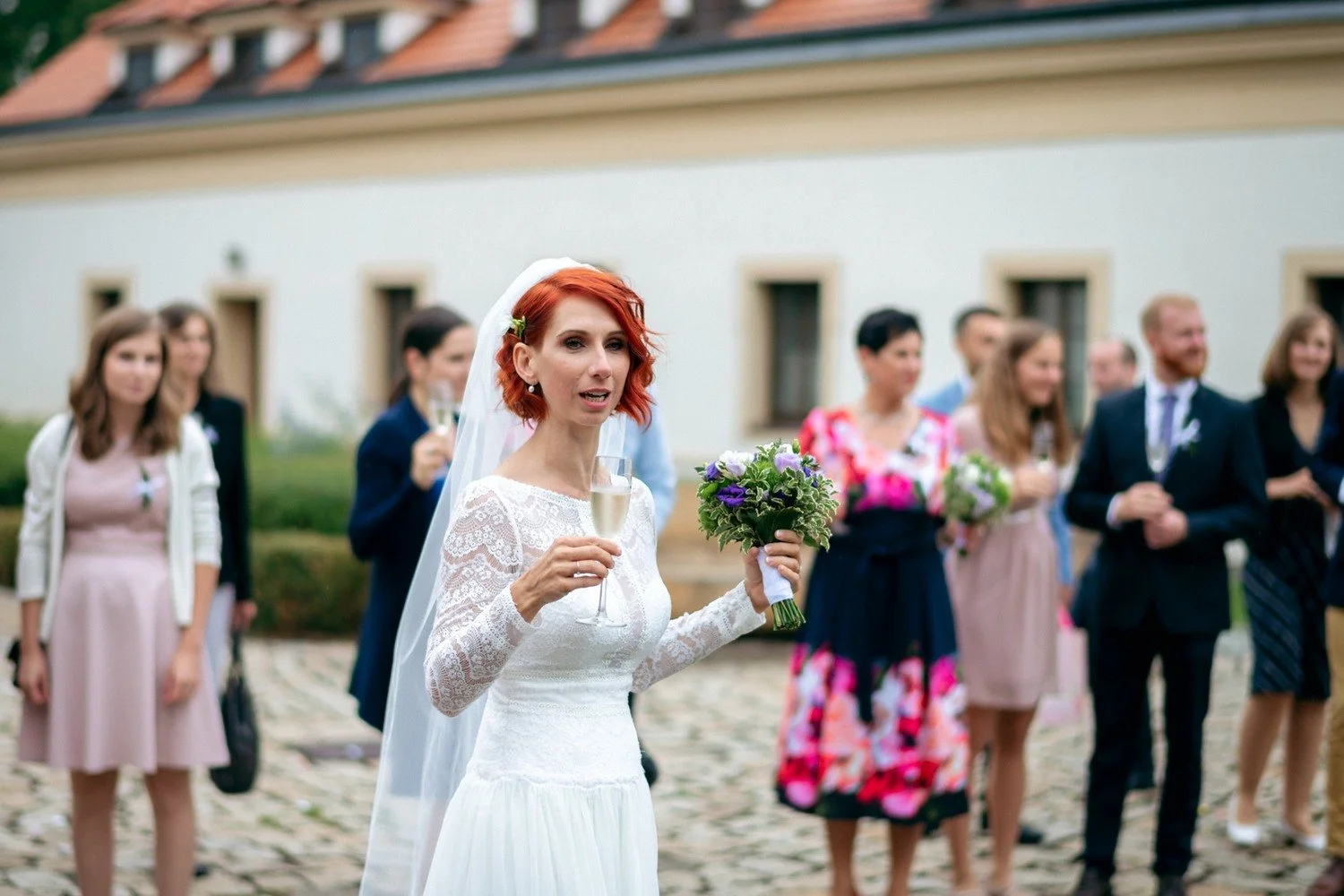 Martina drží kytici a drobný předmět před skupinou hostů.