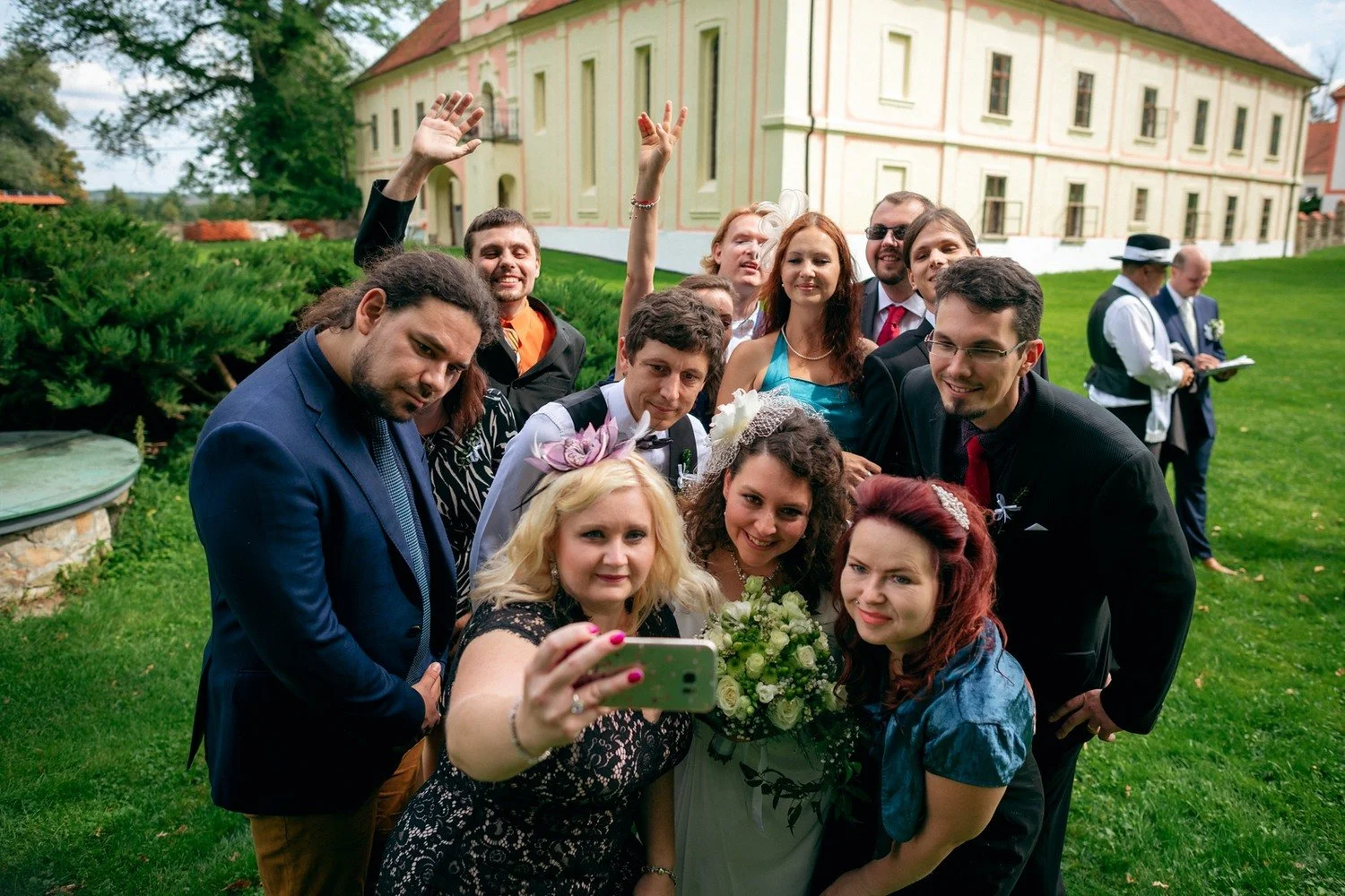 Hosté se sklánějí k telefonu při společném selfie s párem.