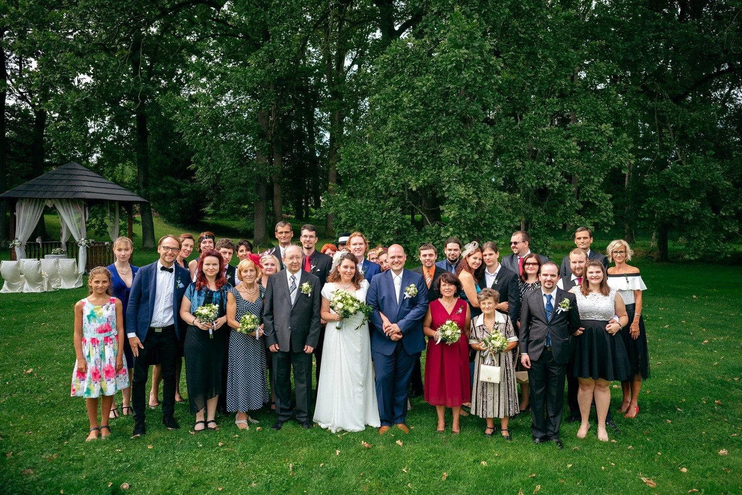 Velká skupina hostů pózuje s párem na trávníku.