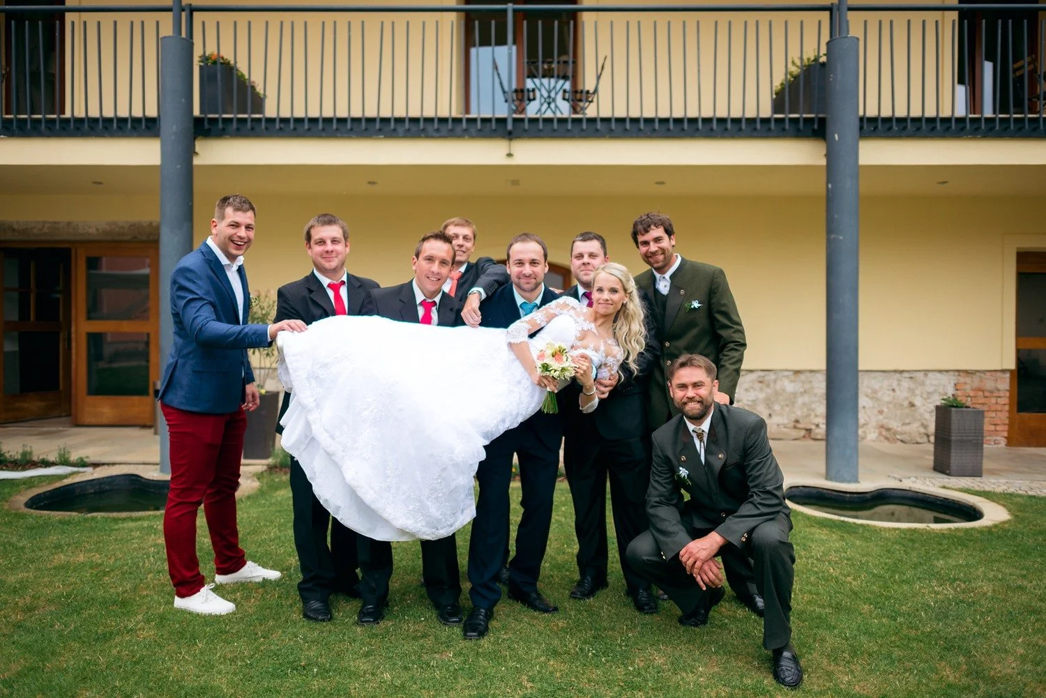 Skupina mužů drží Jitku vodorovně v náručí, zatímco jeden z nich klečí před ostatními.