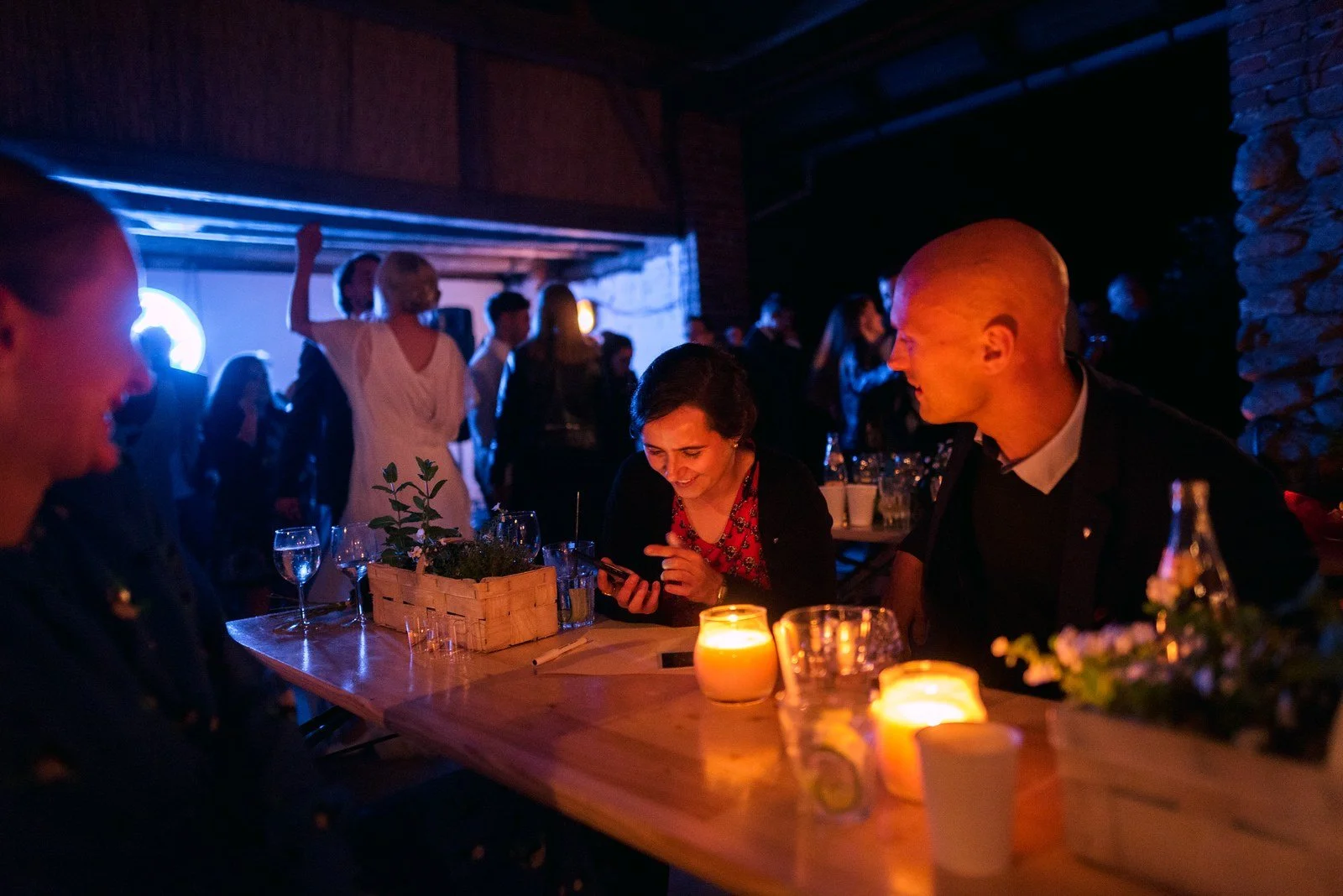 Večerní bar osvětlují svíčky a modré světlo, u pultu sedí několik lidí.