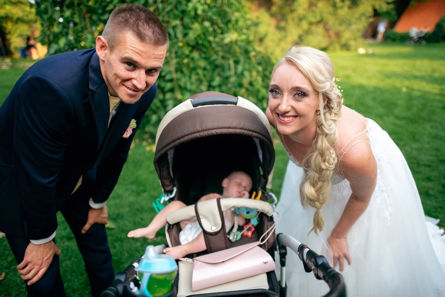 Novomanželé se sklánějí k dítěti v kočárku