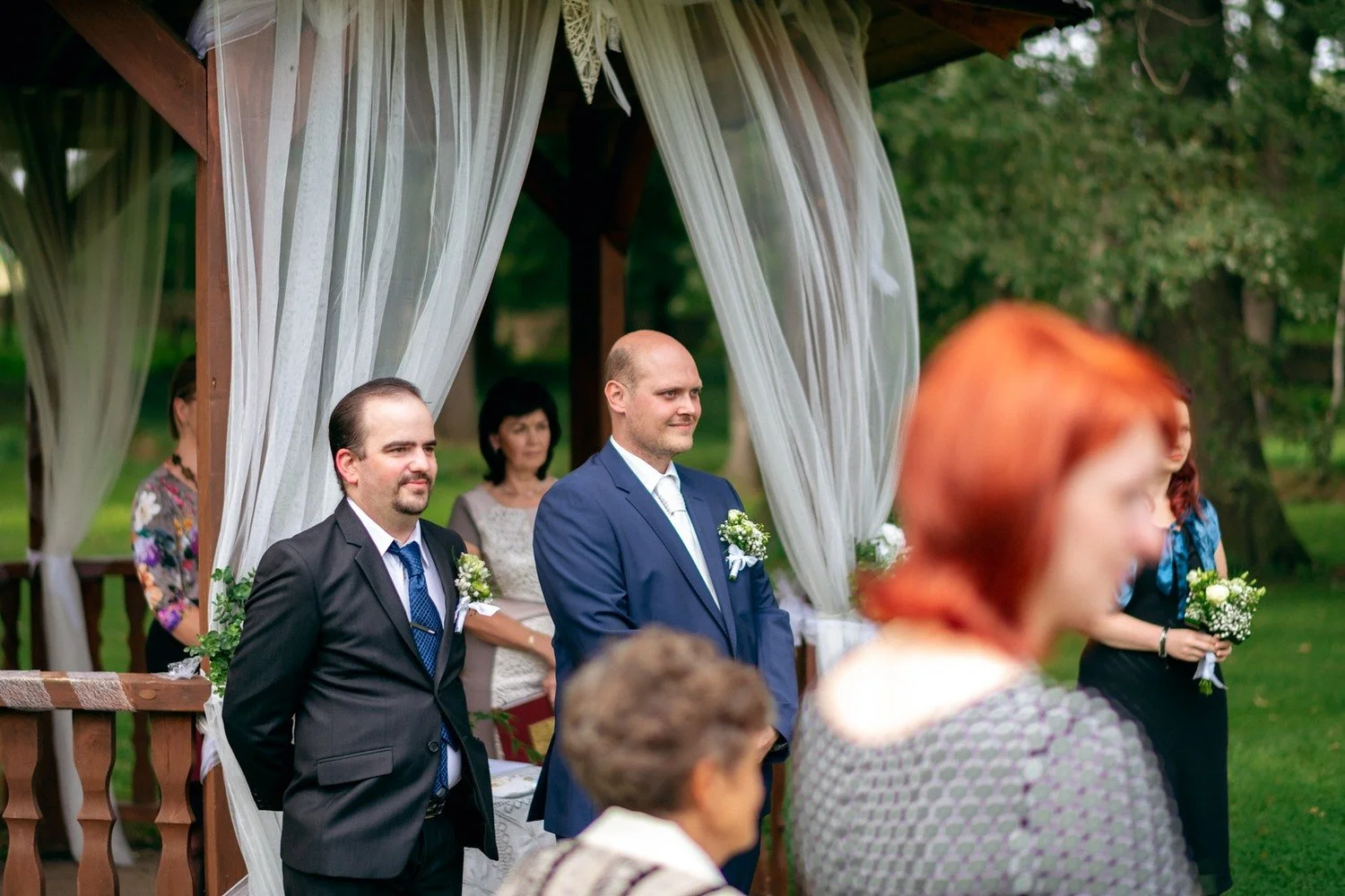Ženich čeká s doprovodem u vyzdobeného altánu.