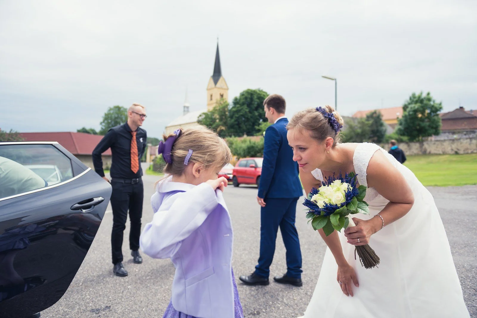 Nevěsta vystupuje z auta a přidržuje si dlouhé šaty.