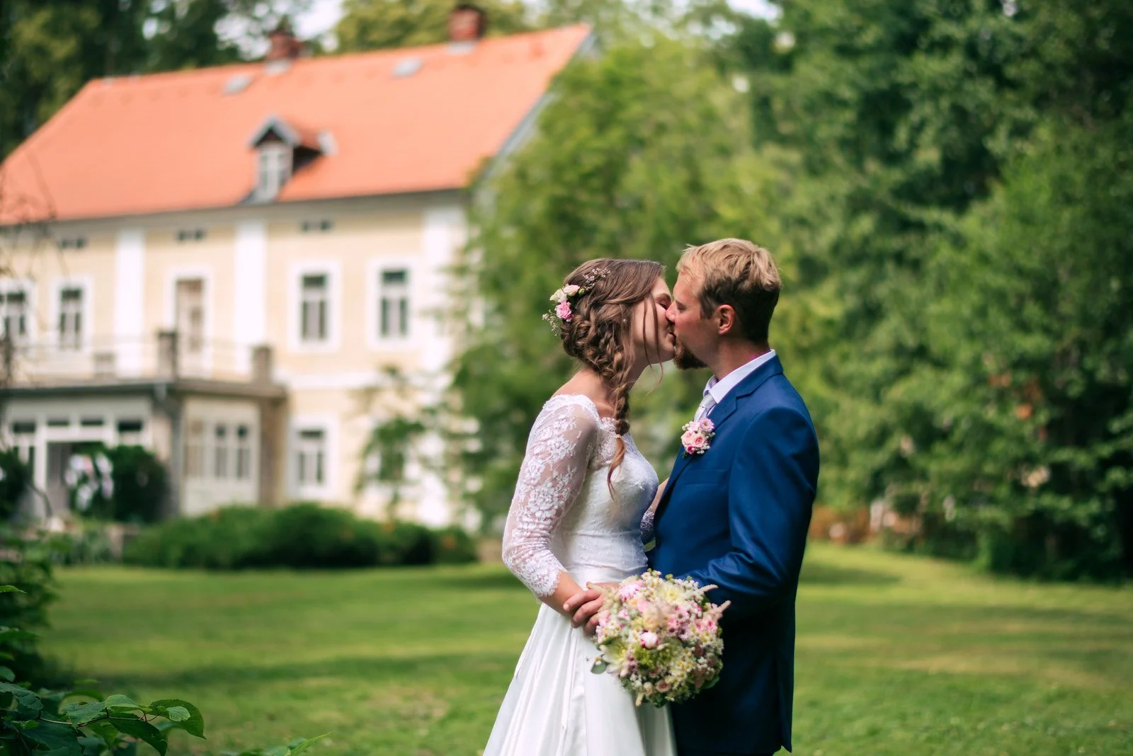 Dvojice stojí těsně vedle sebe na trávníku před budovou.