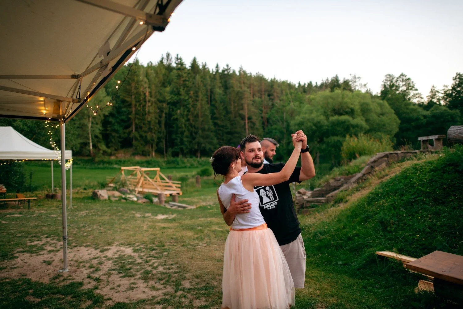 Žena ve světlé sukni a muž v černém tričku spolu tančí u okraje bílého stanu.