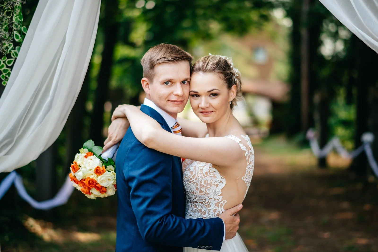 Alex a Fanda se objímají pod bílou látkou zavěšenou mezi stromy.