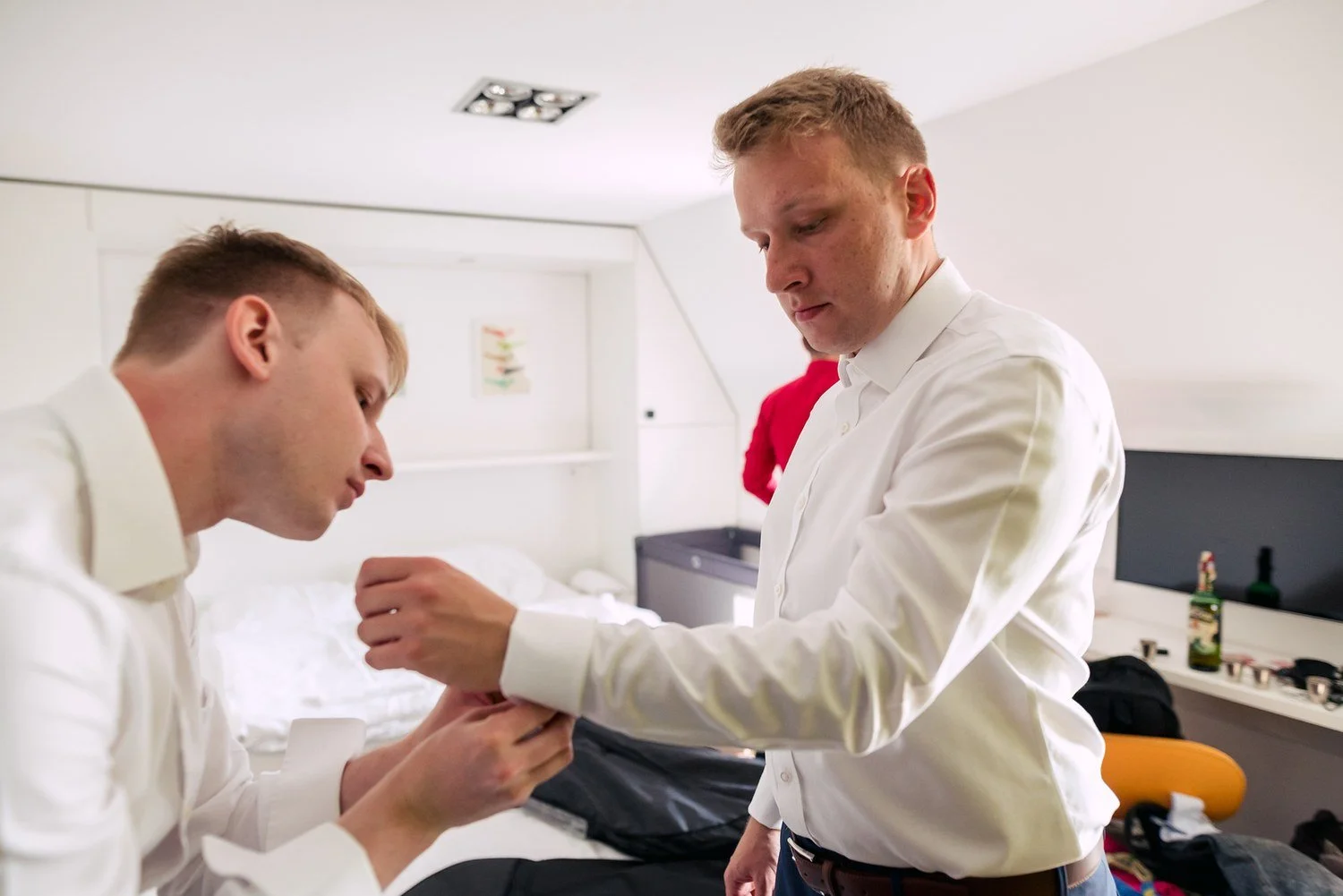 Svědek pomáhá ženichovi při oblékání košile.