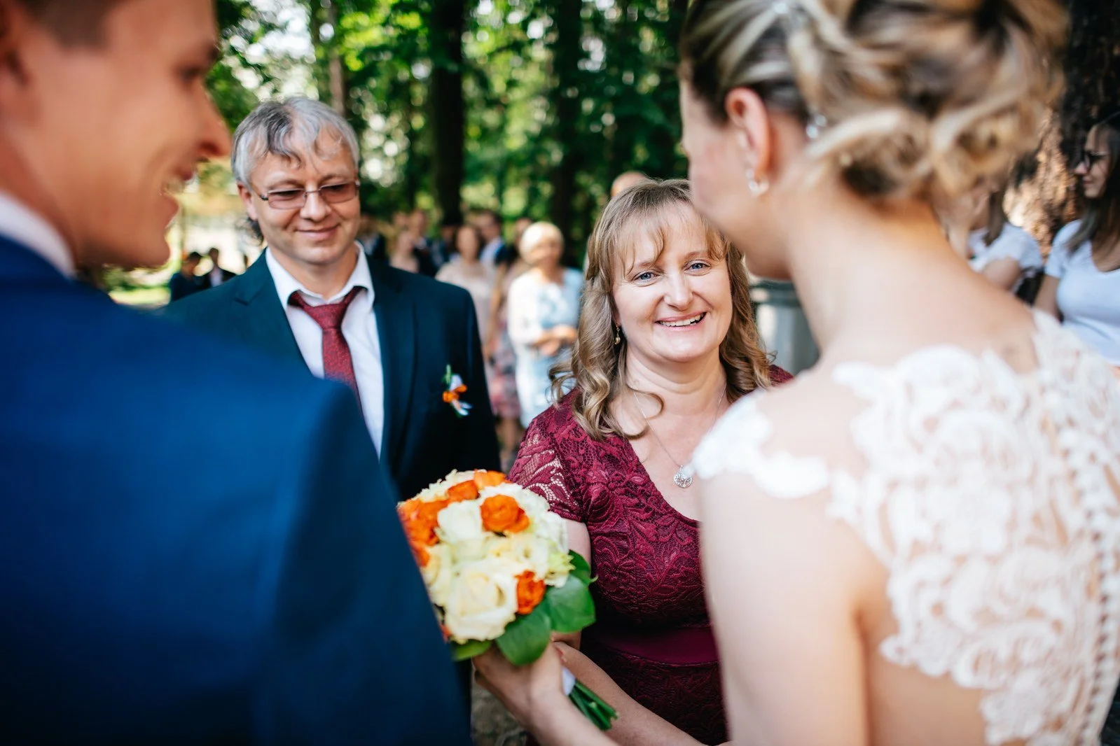 Usmívající se žena sleduje novomanžele zblízka při gratulaci.