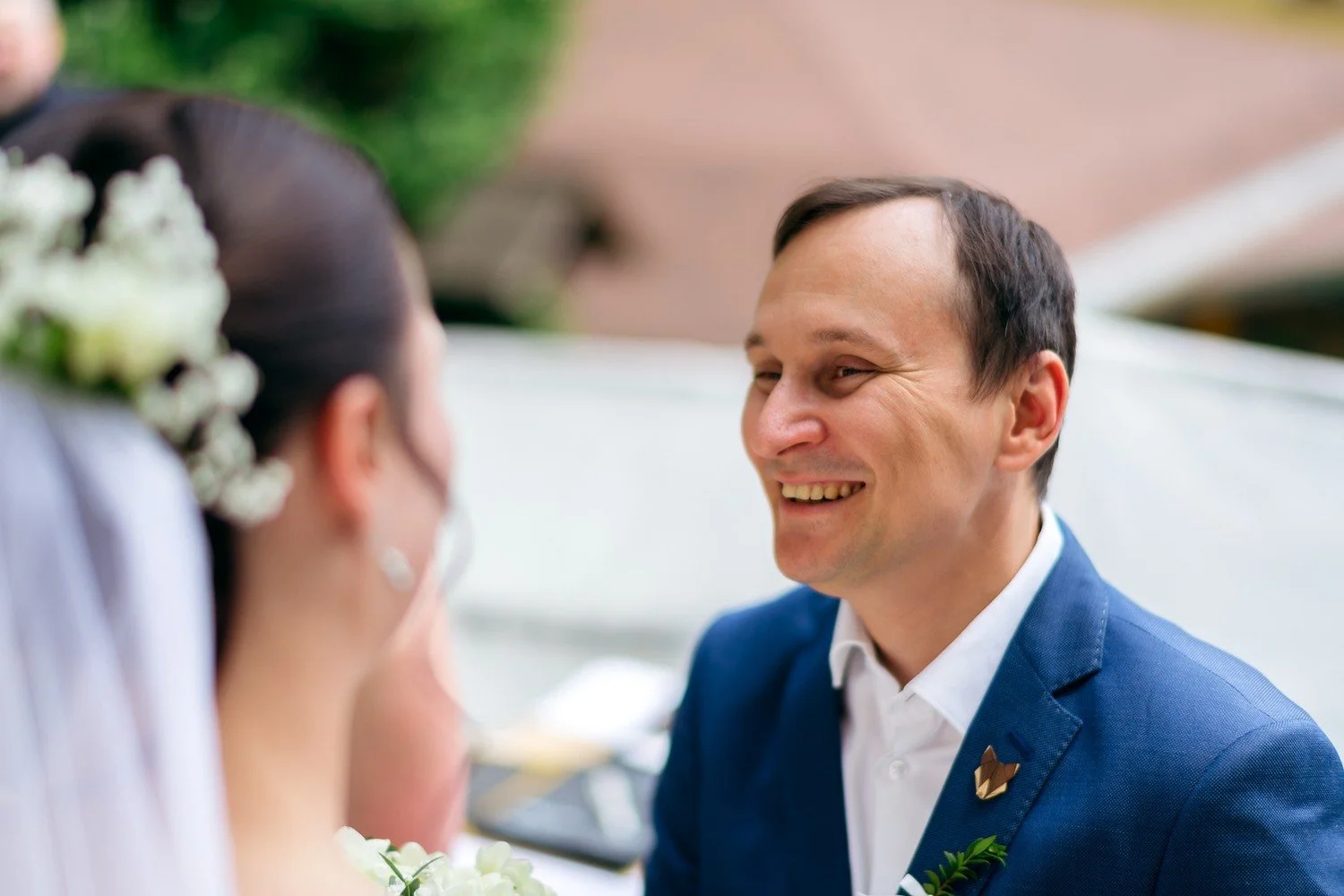 Usmívající se muž v modrém saku hledí k nevěstě v popředí.