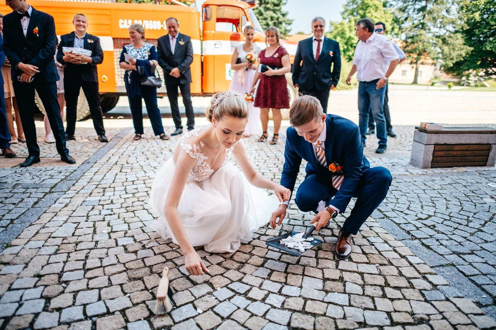 Nevěsta se ženichem zametají střepy z dlažby nádvoří.