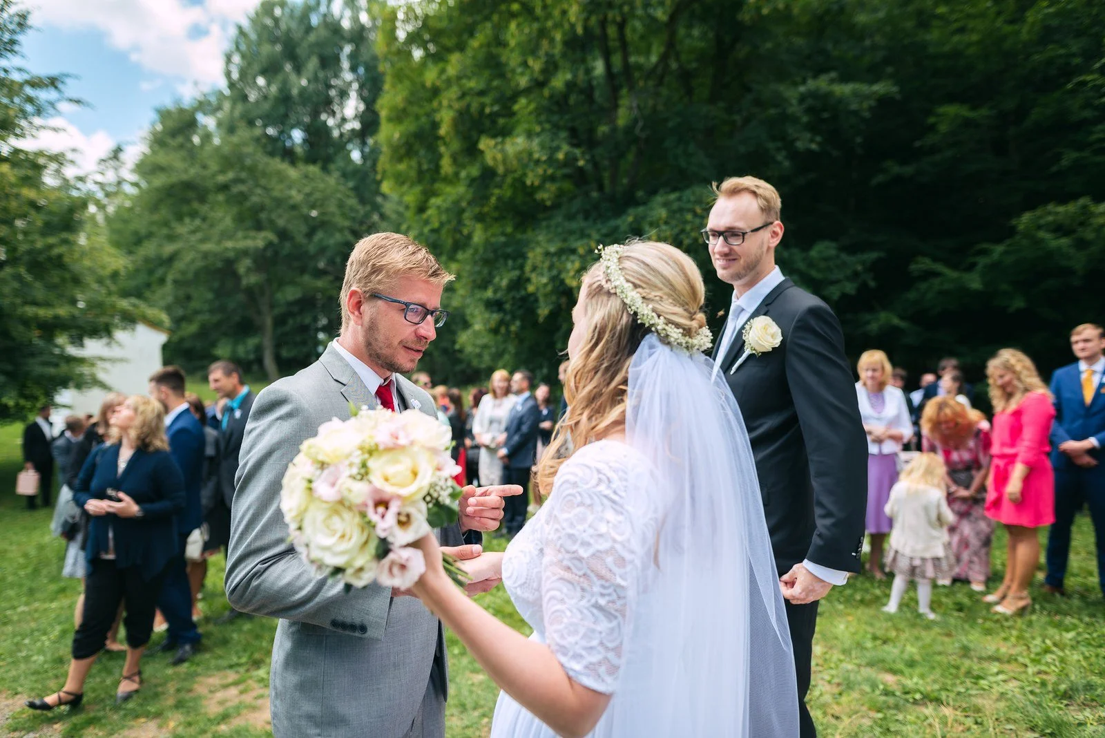 Dvojice stojí ve světlém vchodu do kostela, kolem nich čekají lidé venku.