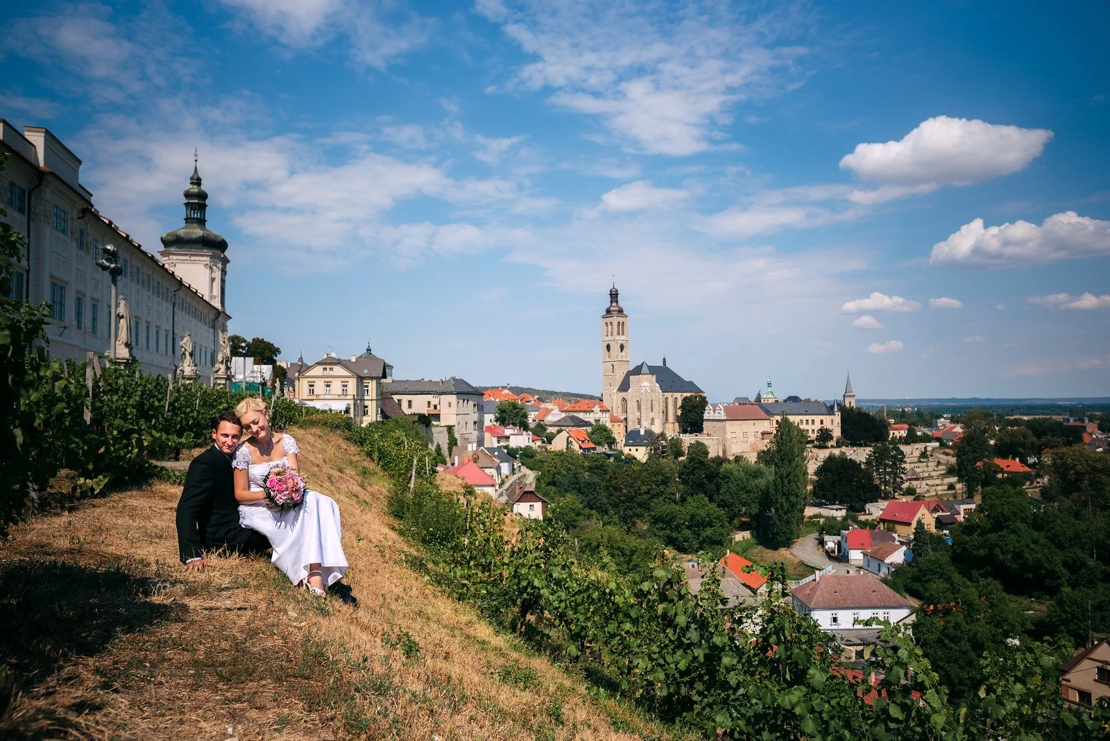 Široký pohled na dvojici ve vinici nad historickým městem.