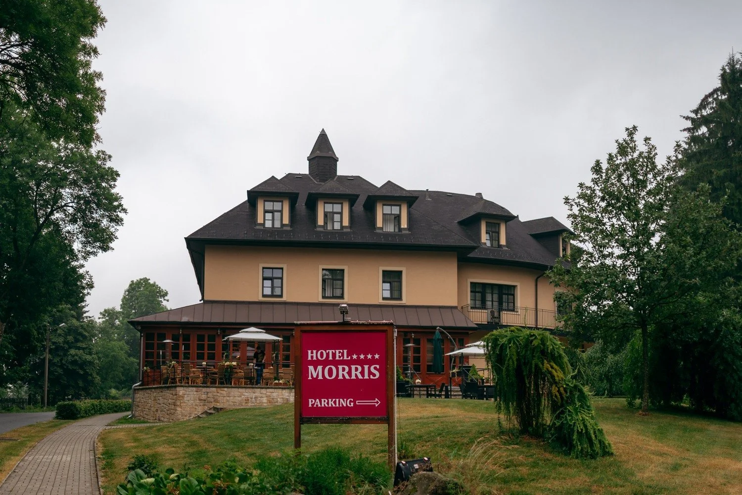 Široký pohled na budovu hotelu Morris se zahradou a červenou směrovkou k parkovišti.