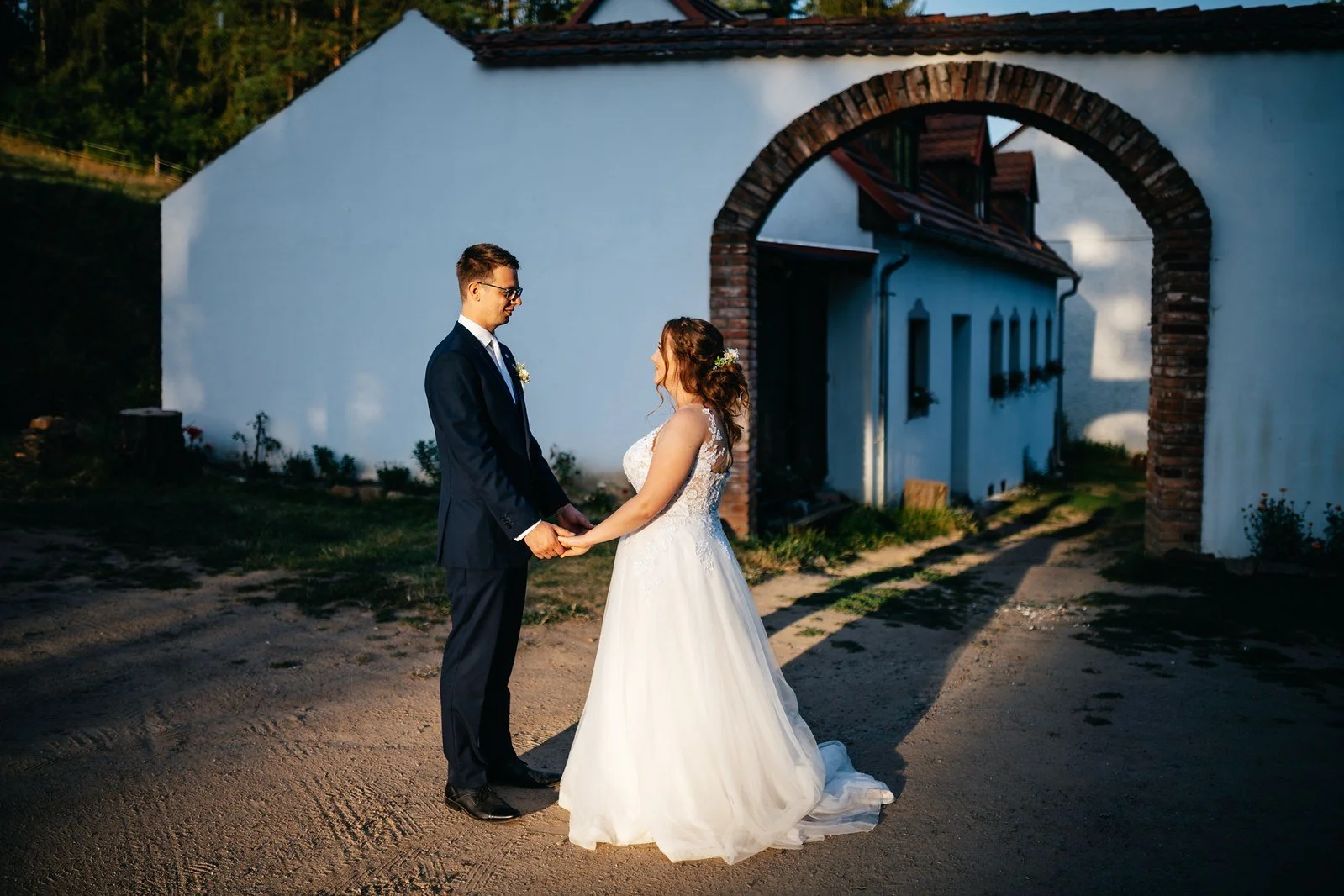 Pár se drží za ruce před vysokou cihlovou branou Uhrovického mlýna.