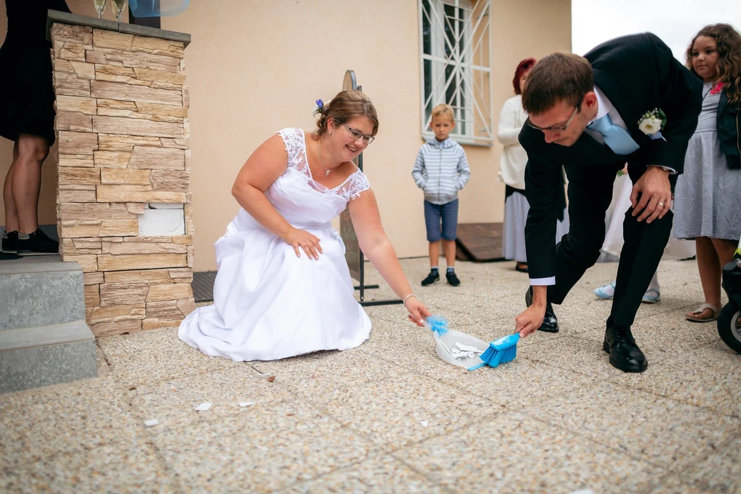Nevěsta a muž v obleku sbírají modré části hry ze země u domu.