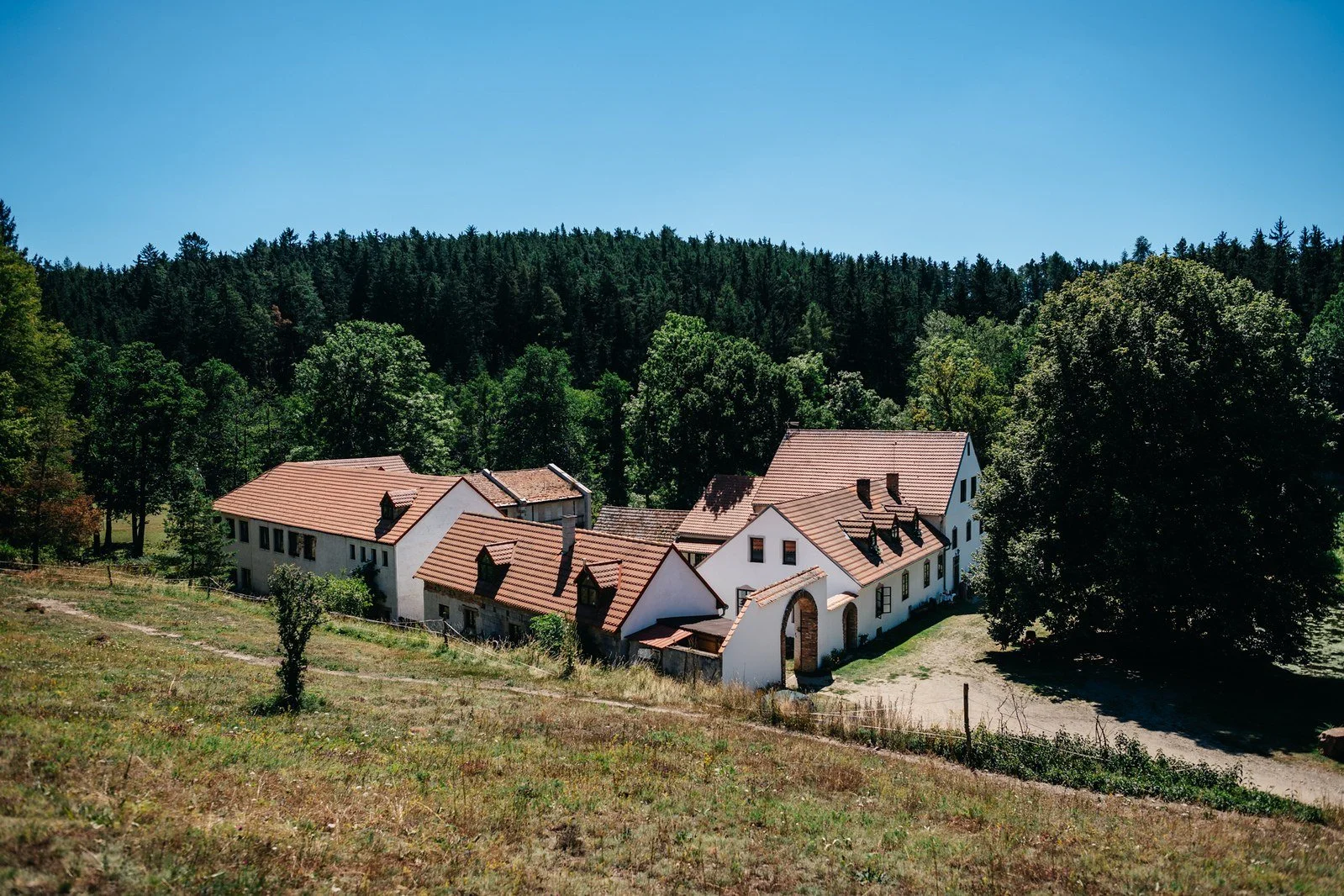 Bílé svatební šaty visí na dřevěném trámu v podkrovním interiéru.