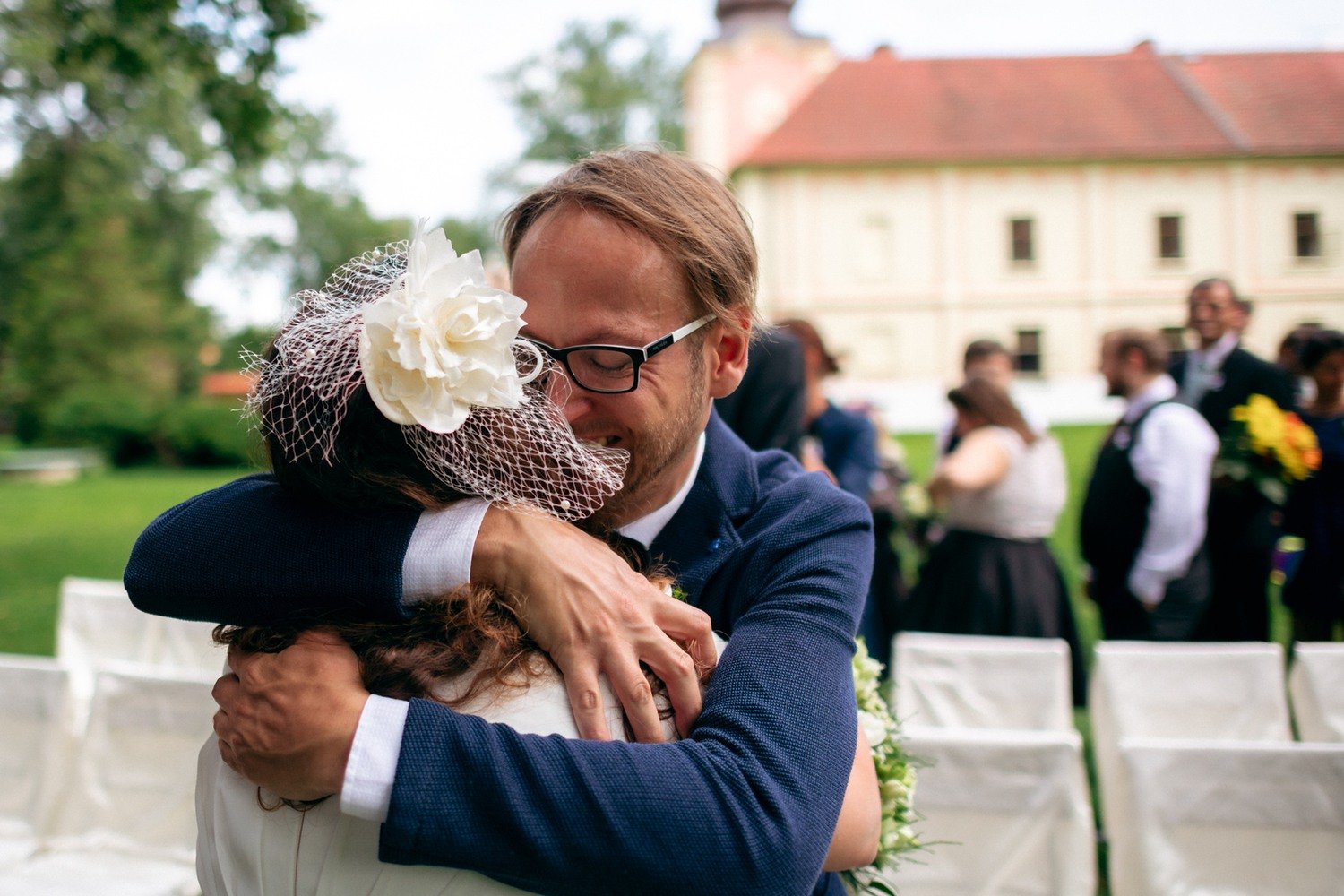 Nevěsta objímá usměvavého muže mezi hosty na zahradě.