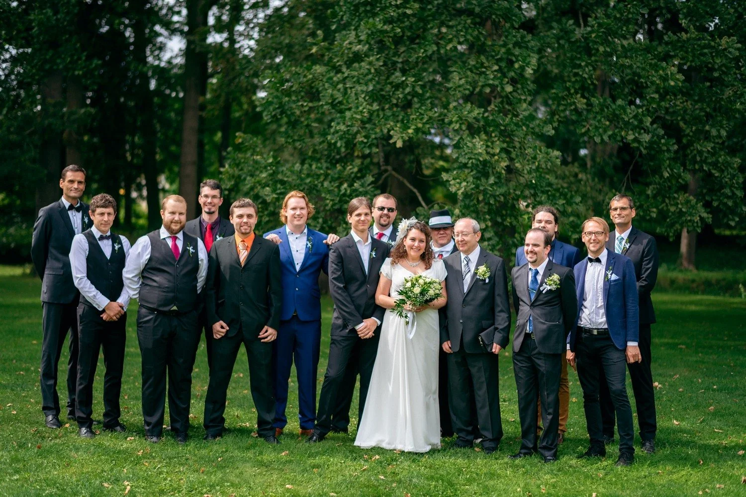 Skupina mužů pózuje s párem před řadou stromů.