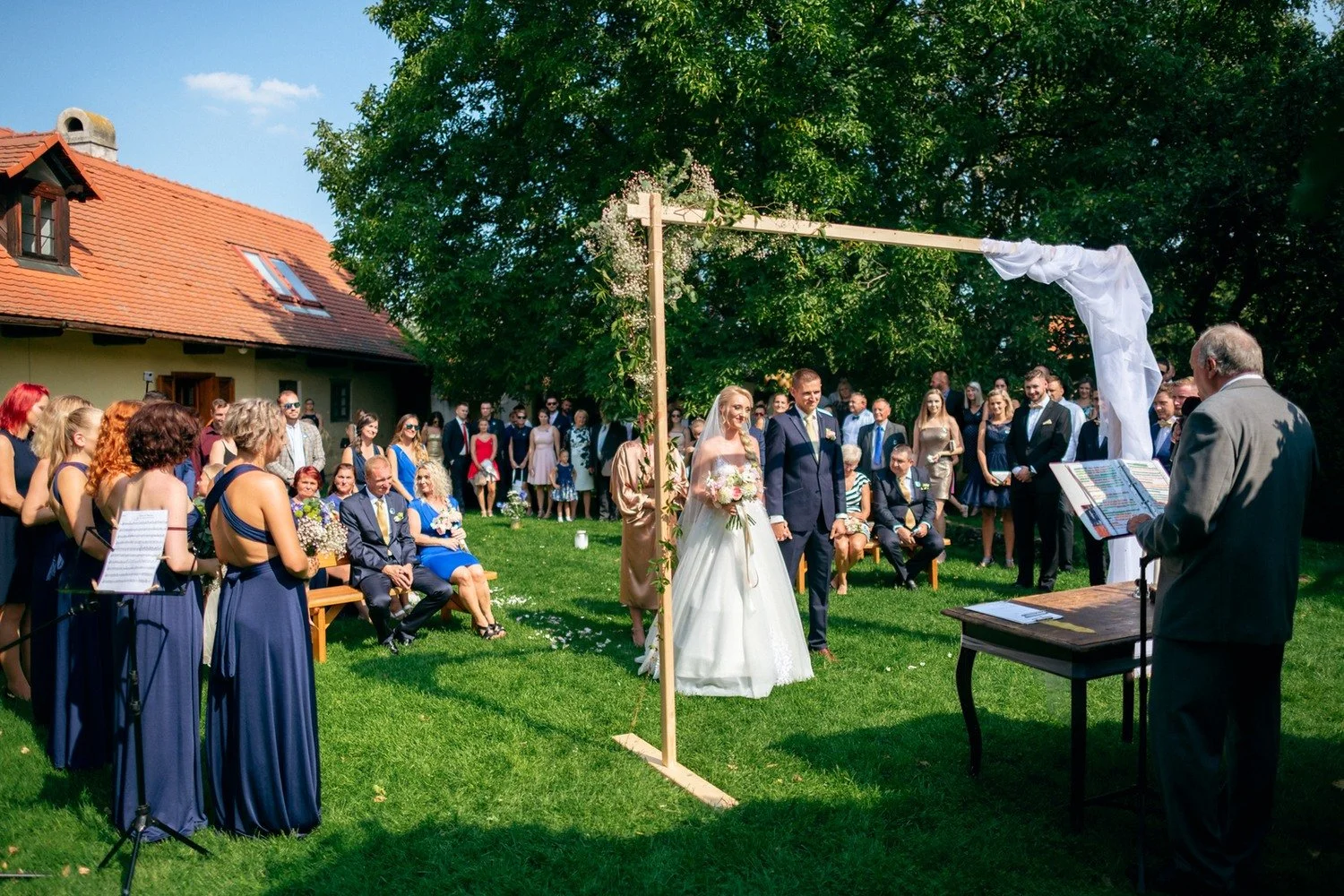 Široký pohled na pár, hosty a zelený obřadní oblouk
