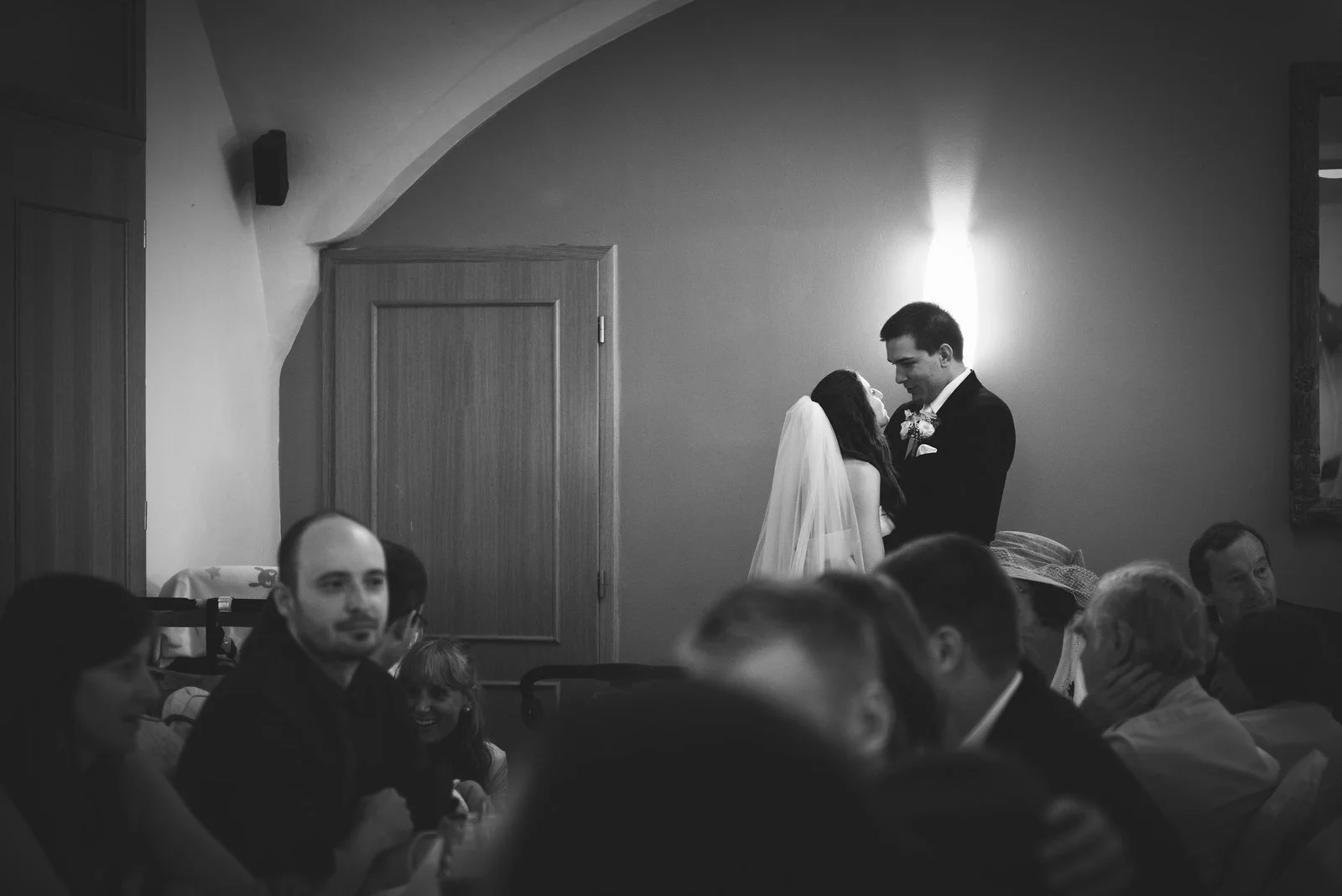 Černobílý nízký záběr řečníka nad siluetami sedících lidí přidává dramatické vrstvení.