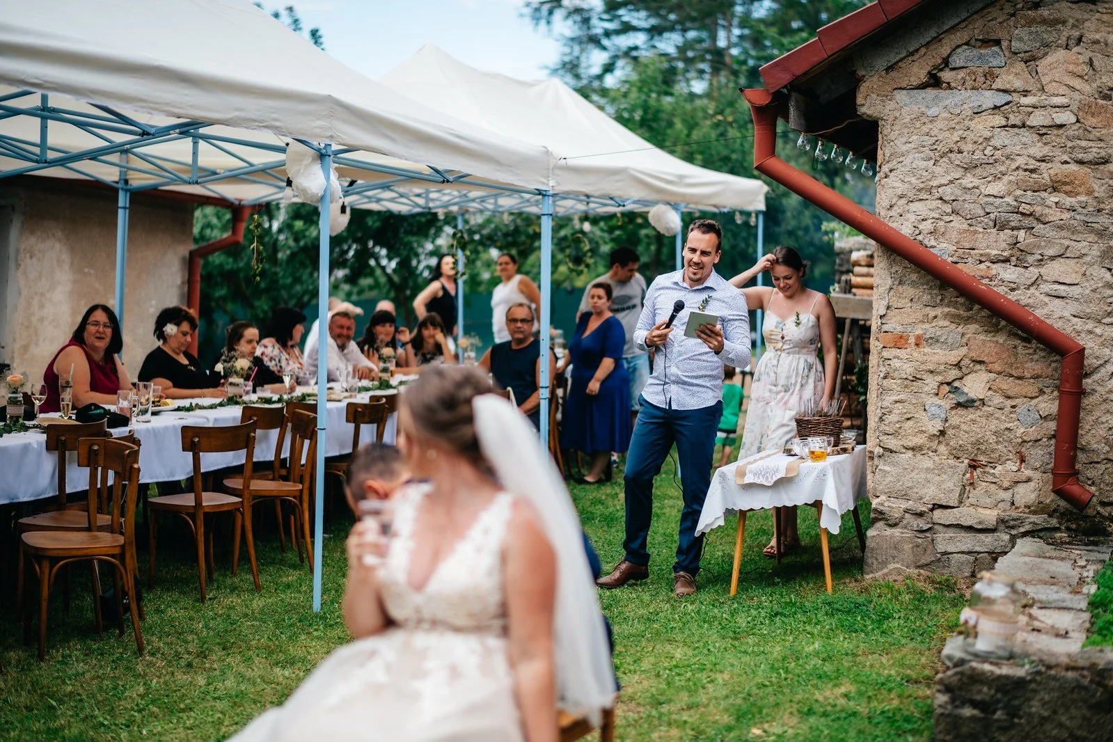 Žena sedí před shromážděnými lidmi; celek vysvětluje další část programu.