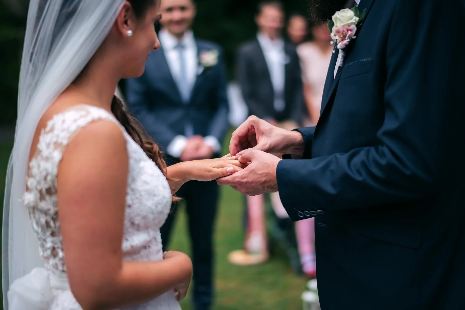 Těsný detail rukou zachycuje výměnu prstenu před rozostřeným publikem.