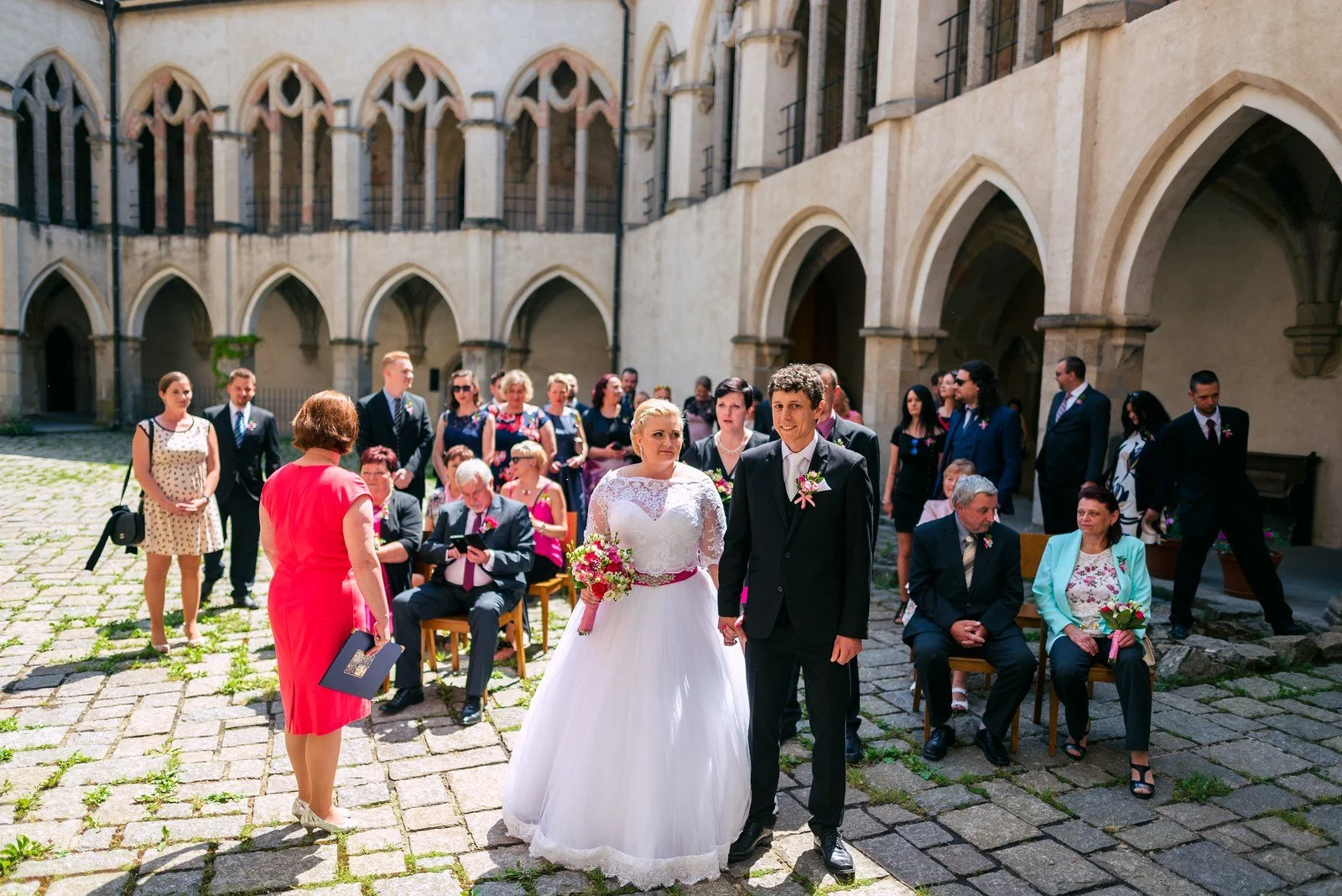 Dvojice prochází středem nádvoří mezi řadami přihlížejících lidí.