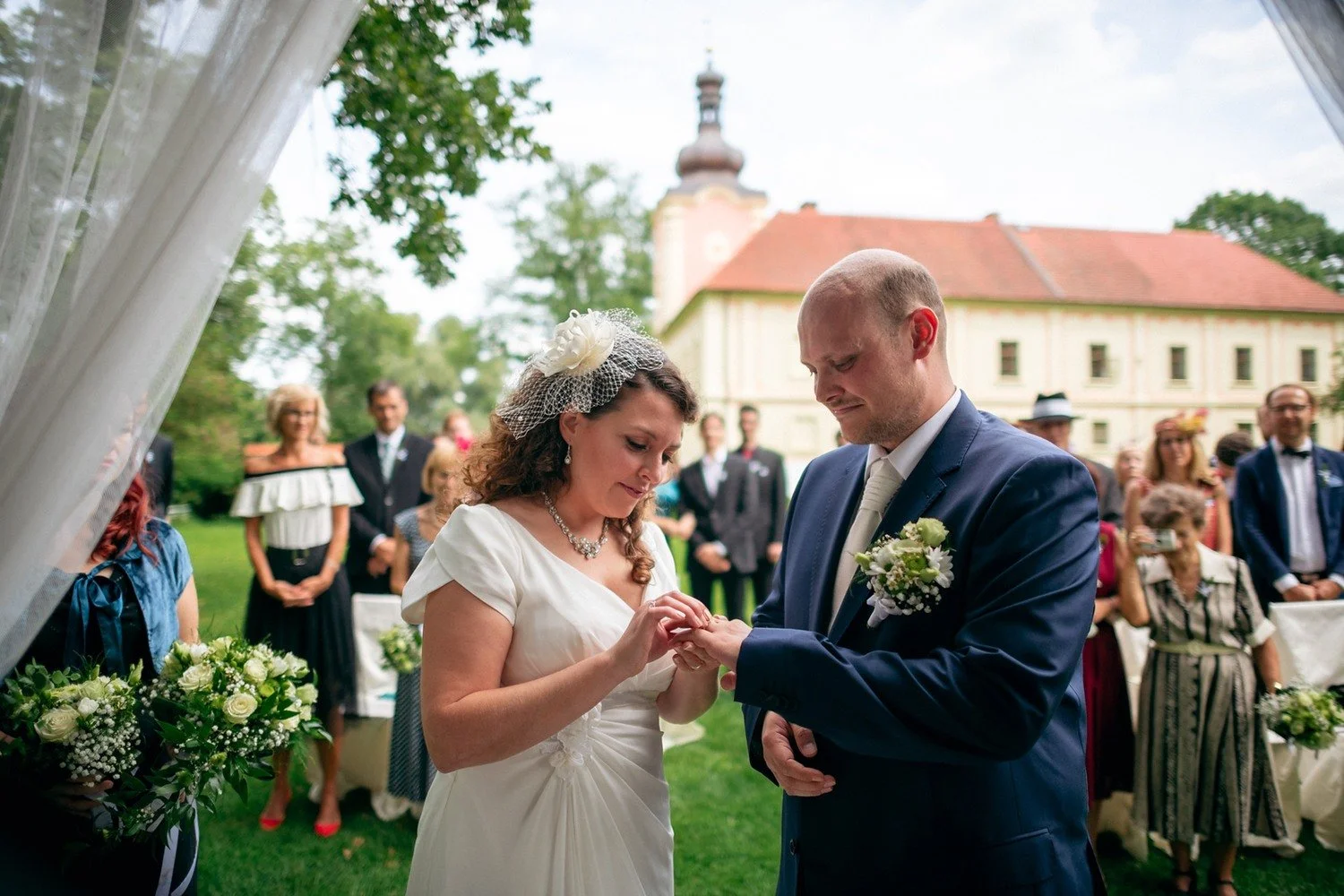 Nevěsta navléká ženichovi prsten před přihlížejícími hosty.