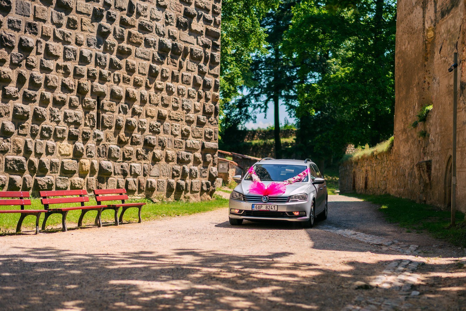 Ozdobené auto přijíždí úzkou cestou podél vysoké kamenné zdi.