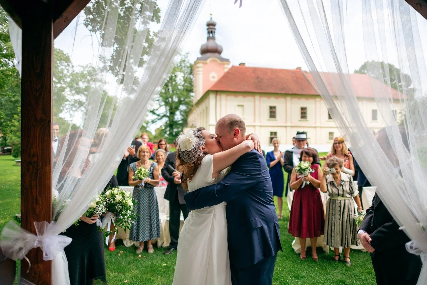 Pár se objímá pod závoji altánu po obřadní chvíli.