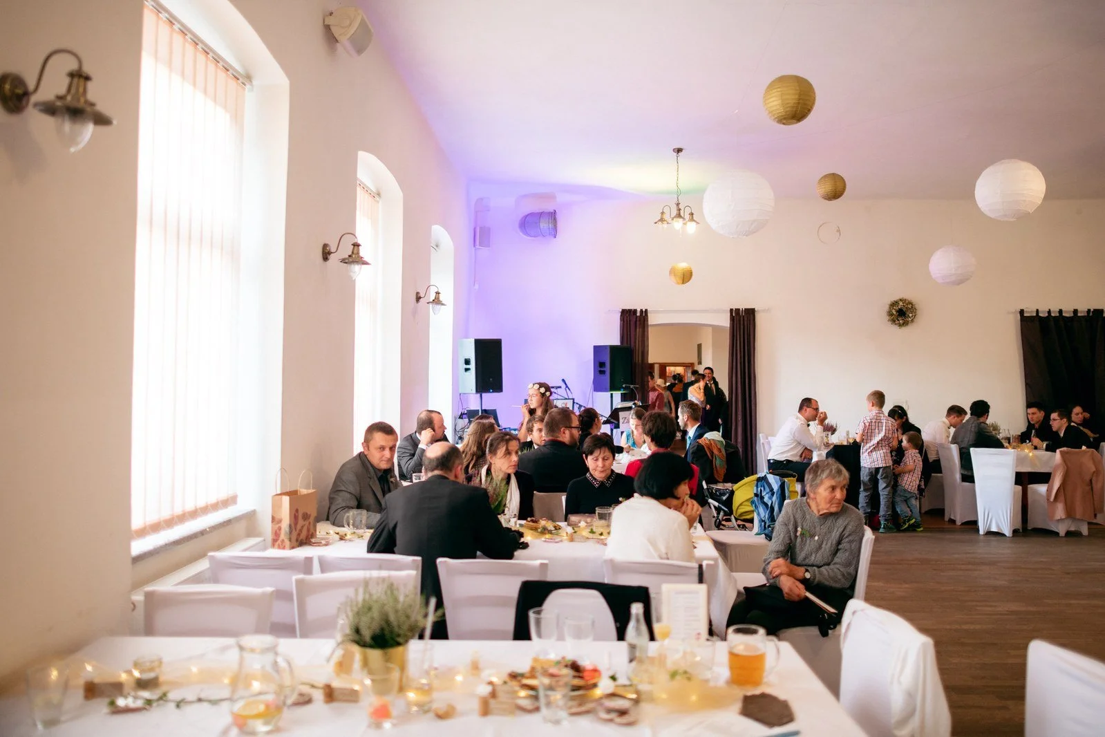 Široký pohled ukazuje hosty sedící u stolů v dlouhém sále nasvíceném fialovým světlem.