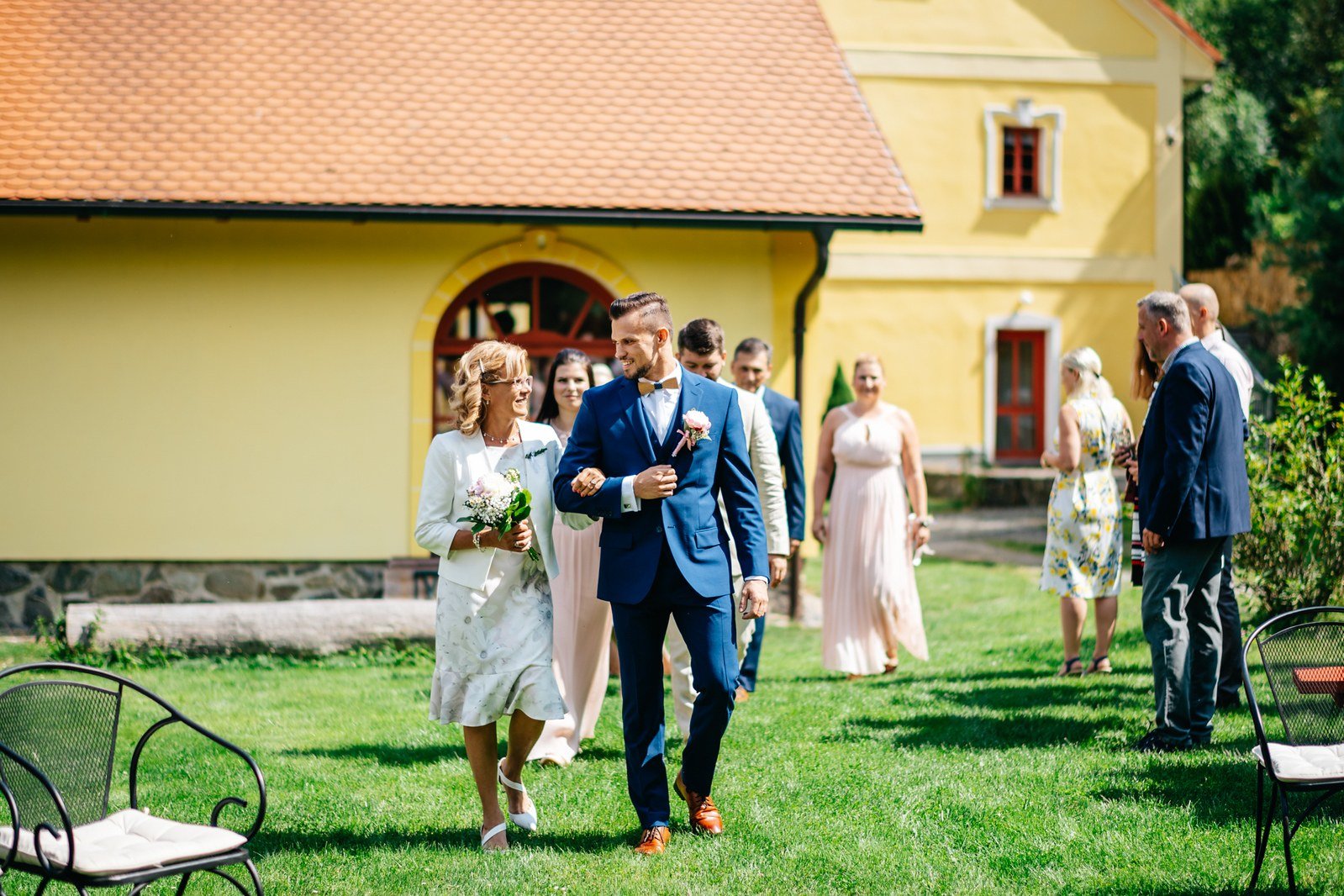 Skupina mužů stojí na trávníku před žlutou budovou mlýna.