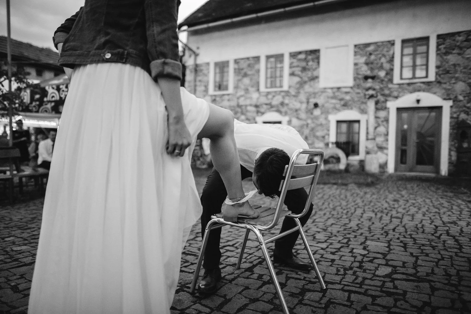 Černobílý snímek zachycuje malé dítě sedící na židli vedle splývající bílé sukně.