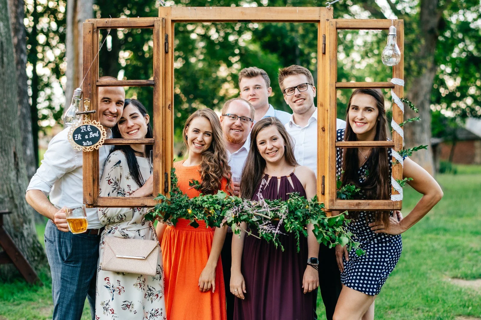 Skupina hostů pózuje s prázdnými dřevěnými rámy v zahradě.