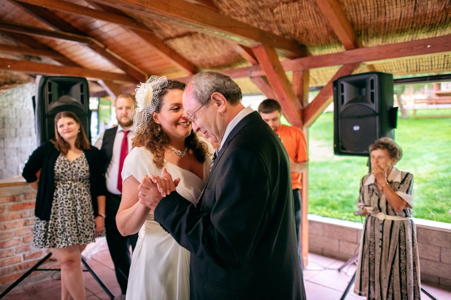Nevěsta tančí se starším mužem v zahradním pavilonu.