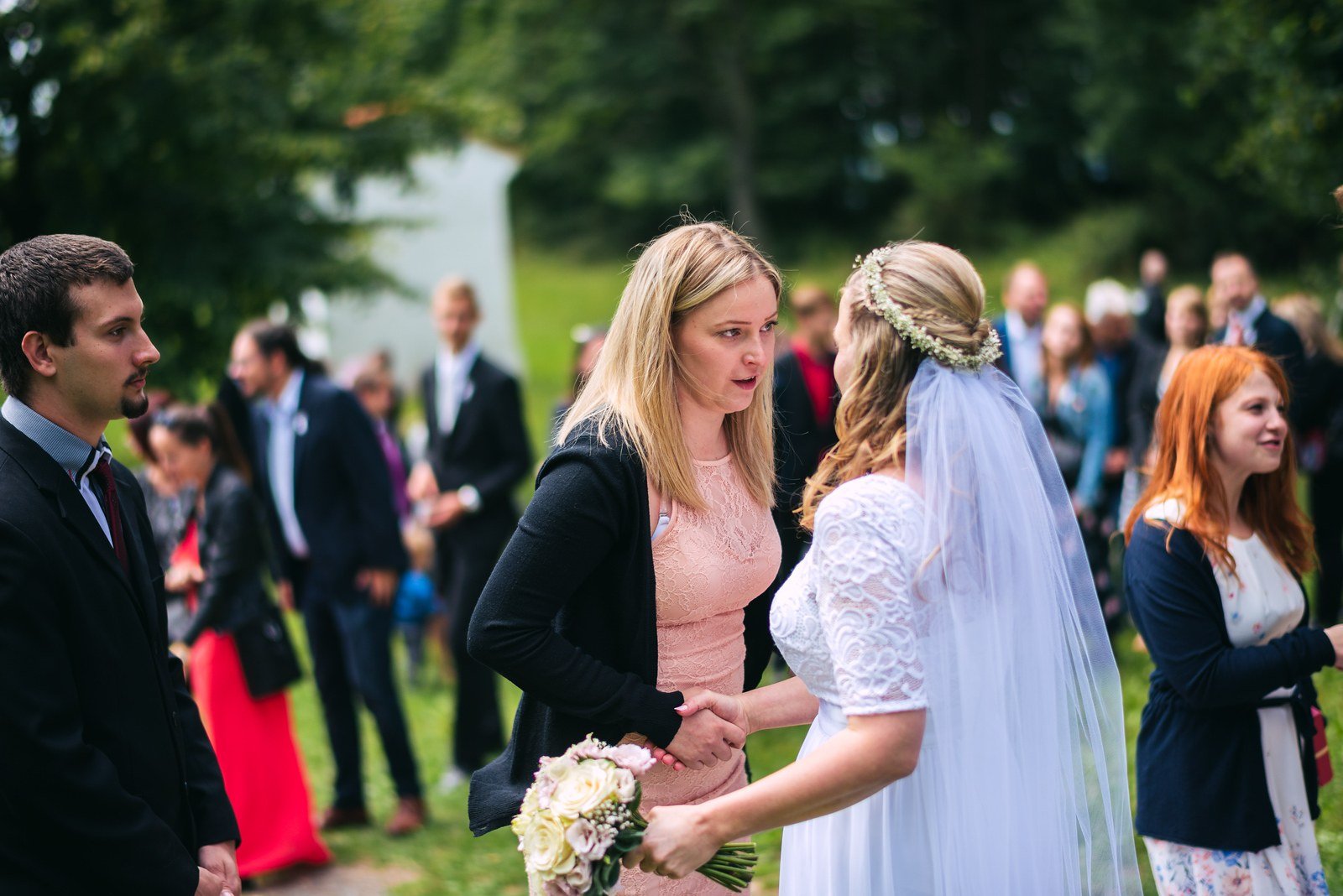 Žena v bílých šatech a muž v tmavém obleku vycházejí z kostela mezi řadou hostů.