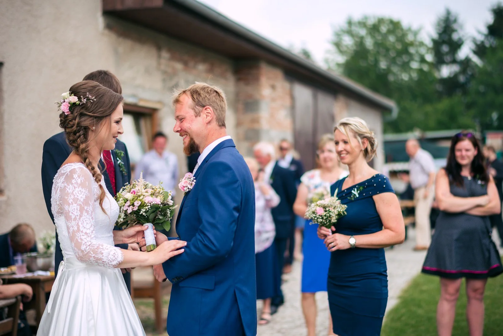 Žena v bílých šatech přebírá venku světlou kytici.