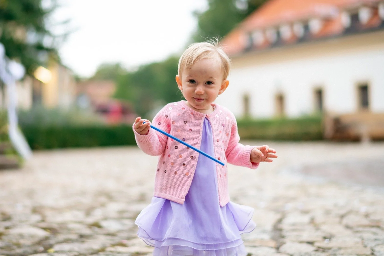 Malá dívka v růžové vestě drží venku modrou hůlku.