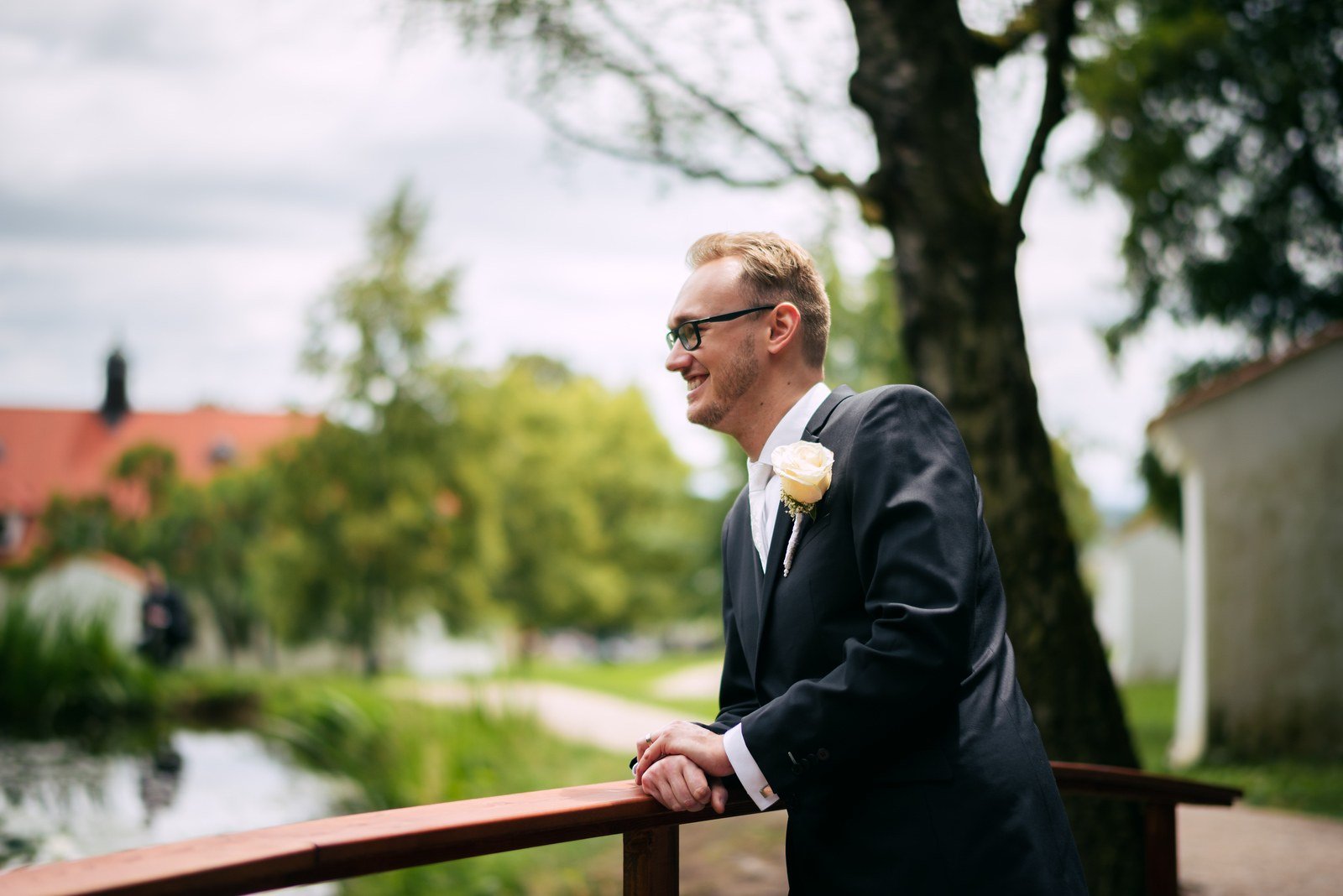 Muž v tmavém obleku a žena v bílých šatech pózují spolu na lesní cestě.
