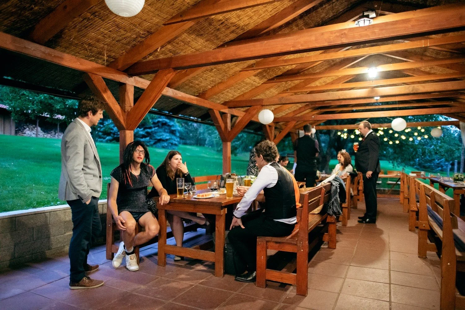 Hosté sedí a stojí v osvětleném pavilonu po setmění.